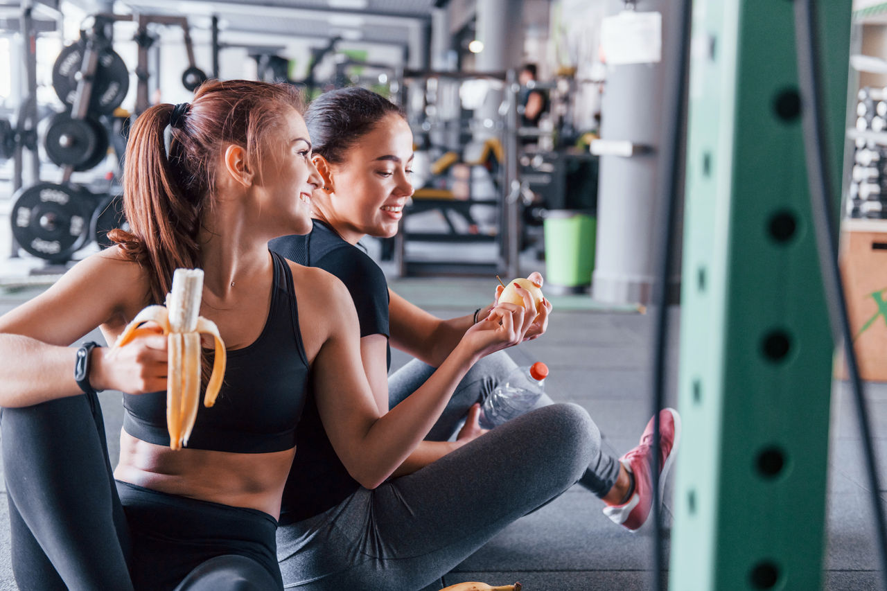 Two female friends in sportive clothes is in the gym earing fruits and taking a break.; Shutterstock ID 1585672012; purchase_order: POIIG0004097; job: OMG1193295; client: Danone UK; other: 480